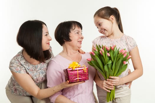 the daughter and the granddaughter give a bouquet of tulips to the grandmother