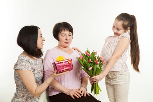 the daughter and the granddaughter give a bouquet of tulips to the grandmother