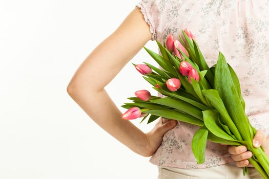 the girl holds a bouquet of tulips behind the back