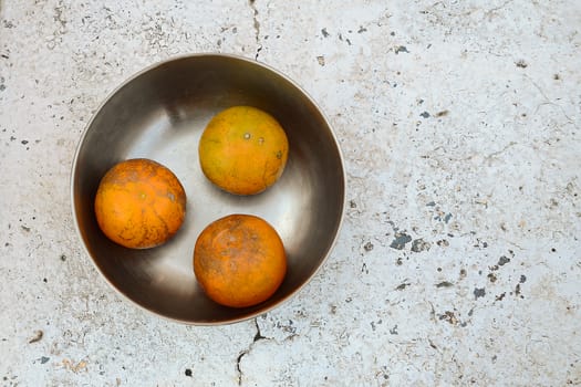 tree oranges in stainless steel bowl on white stone table