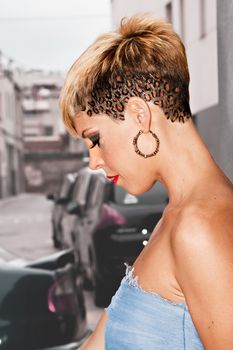 Young woman in style of urban fashion. Short blonde leopard skin hairstyle. Dressed with a blue dress. Urban fashion photography. Vertical image.