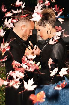 Romantic fashionable young couple caught with blowing leaves. Urban fashion photography. Vertical image.