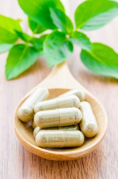 Herbal medicine capsules in wooden spoon with green leaf on wooden background.