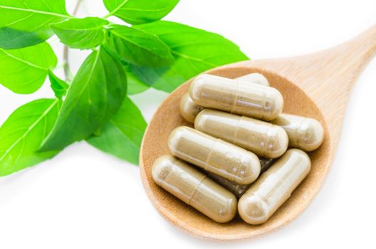 Herb capsule medicine in wooden spoon and green leaf on white background.