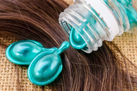 Hair vitamin serum capsule with damaged hair on sack background.