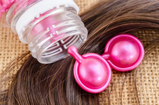 Hair vitamin serum capsule with damaged hair on sack background.