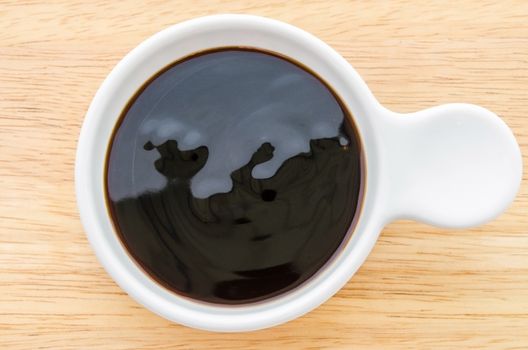 Oyster sauce in white bowl on wooden background.