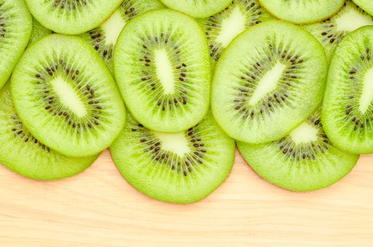 Many slices of kiwi fruit on wooden background.