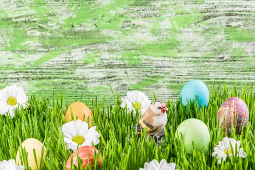 Easter background with eggs in grass and flowers, wooden backdrop