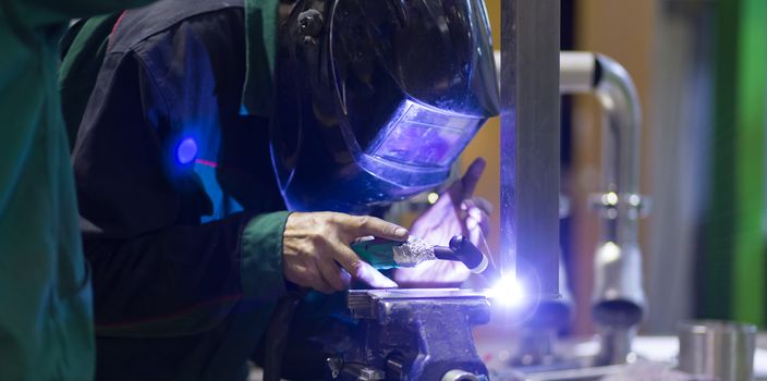 Industrial worker with protective mask welding inox elements in steel structures manufacture workshop.