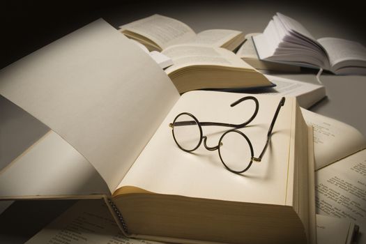 Pair of reading glasses on top of an open book, near other open books