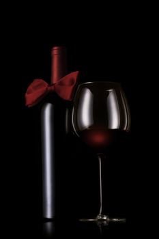 A red wine bottle with bow tie next to a wine glass on black background