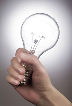 Hand holding a light bulb on grey background