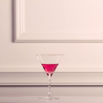 Lonely cocktail glass with pink liquid against an elegant wall.