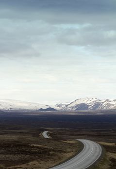 Vertical photo of a winding asphalt road going into the mountains in Thingvellir national park in Iceland