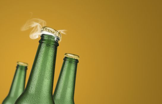 Horizontal photo of three green cold beer bottles with water drops and golden cap open on yellow background