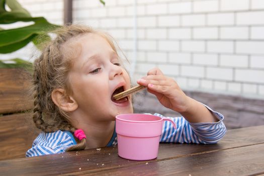 Four-year girl sitting at a wooden table on the porch, and breakfast