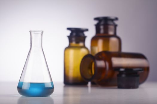 A medical glass with blue liquid in front of old brown jars