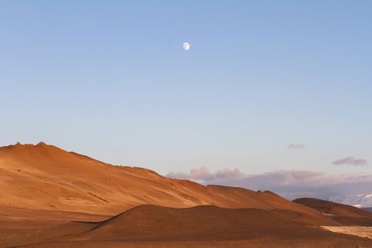 Horizontal view of ash volcanic mountains with blue sky and moon above near Myvatn baths in Iceland