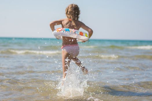 Six year old girl running to swim in the sea, focus on a spray of water