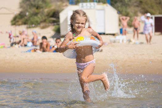 Six-year girl runs with a swimming circle swim in the sea