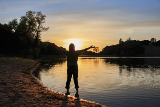 Young Girl Watching the Sun Set With Hands Raised High