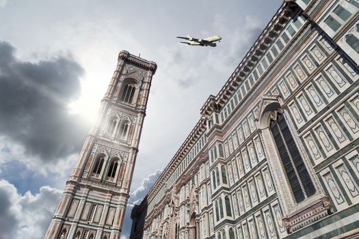 Bottom view of belfry tower of Florence Duomo, Santa Maria Del Fiore, on cloudy grey sky background with a plane.