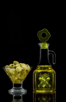 The olives in the bowl and oil in the bottle, on black background.