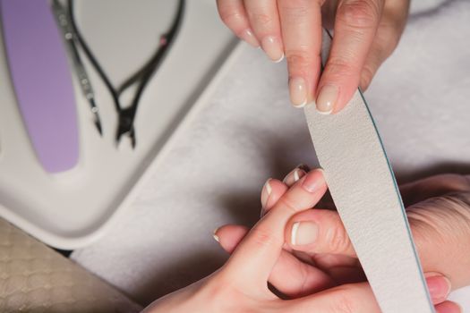 Closeup shot of a woman in a nail salon receiving a manicure by a beautician with nail file. Woman getting nail manicure. Beautician file nails to a customer.