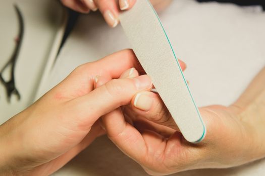 Closeup shot of a woman in a nail salon receiving a manicure by a beautician with nail file. Woman getting nail manicure. Beautician file nails to a customer.