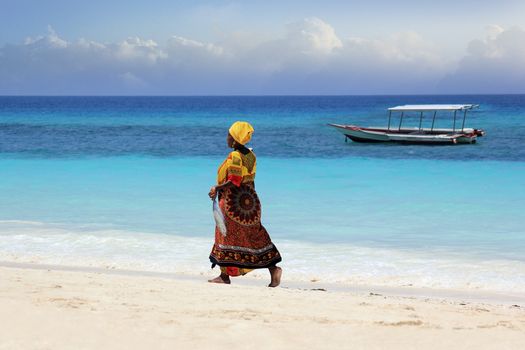 Zanzibar, Tanzania - January 7, 2016: An African woman in traditional dress with fish walks down the beach. Zanzibar, Tanzania