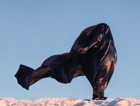 View of a dark figure covered in fabric on the wind on a salt hill.