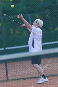 Senior man playing tennis on a gravel court