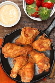 Chicken Wings in Skillet with Strawberries and Sauce on table.