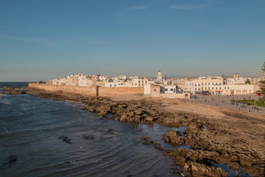 Sky view on the city Essaouira. Waves of the Atlantic ocean. Rocky coast. Houses of the old city, minaret of a mosque. Blue sky.