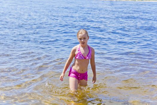 Cute girl in pink swimsuit on water background