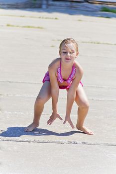 Cute jumping girl on the riverbank in pink swimsuit