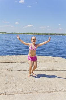 Dancing girl on the riverbank in pink swimsuit