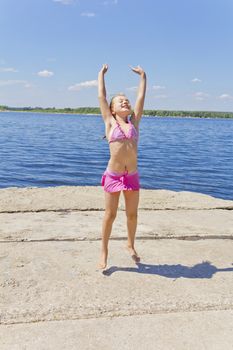 Cute jumping girl on the riverbank in pink swimsuit