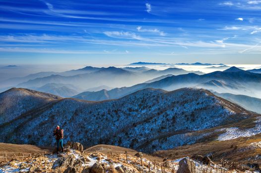 Young woman hiker taking photo with camera on mountains peak in winter.