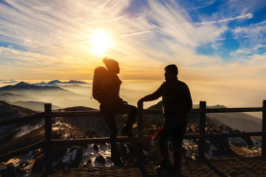 Silhouette of young woman and man with backpacks and sticks on mountains at sunset.