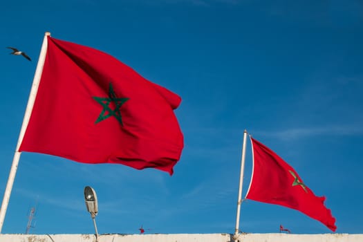 Two morrocan flags blowing in the wind. Blue sky.