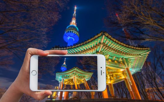 Hand holding smart phone take a photo at Seoul tower at night.