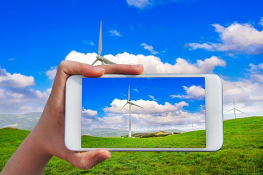 Hand holding smart phone take a photo at Wind turbines generating electricity.