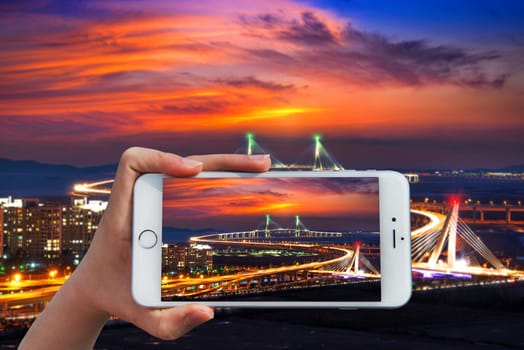 Hand holding smart phone take a photo at incheon bridge with sunset