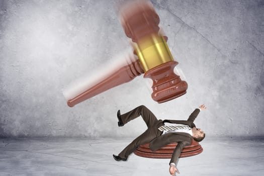 Inscribed gavel hitting scared businessman on grey wall background, justice concept