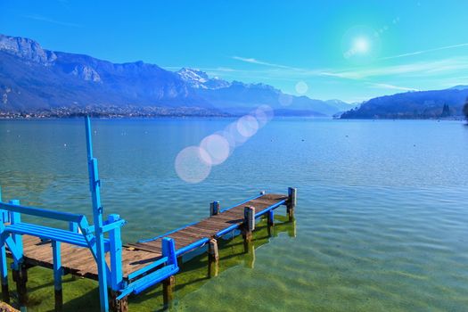 Blue wooden pontoon on Annecy lake and Alps mountains by beautiful day, France
