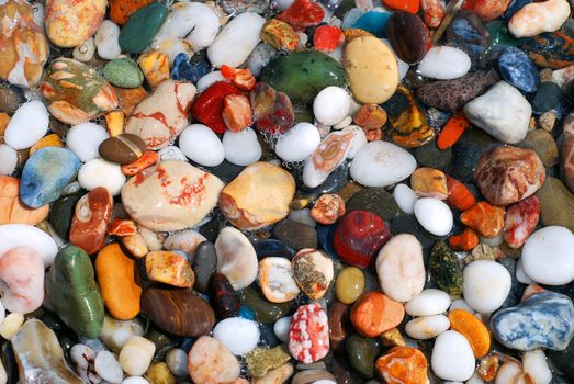 Multicolored sea pebbles in the water on the shore for background or wallpaper.
