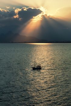 Silhouette of sailboat in Antalya bay, Turkey, at sunset with Bydaglari Mountains in the background.