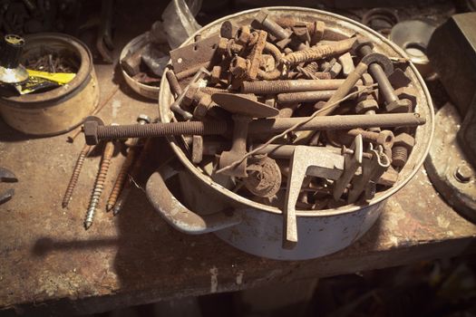 Old metal screws and nuts in an old saucepan in an abandoned workshop

